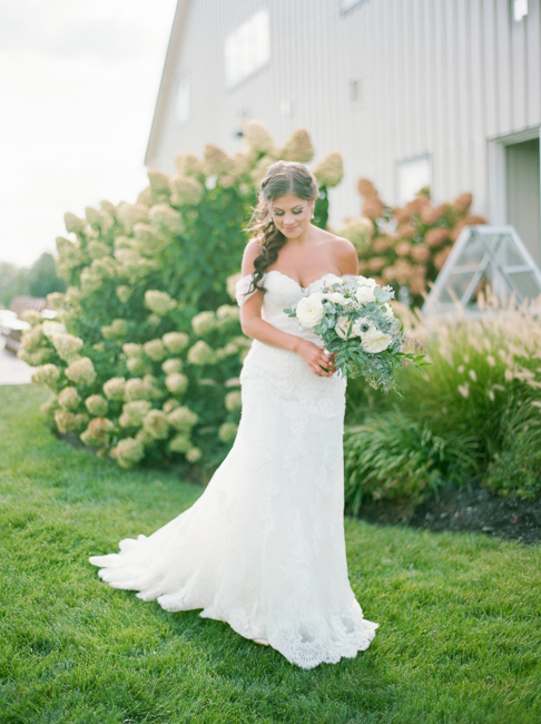 bride standing with bouquet by garden 