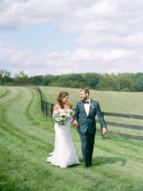 bride and groom walking by field 